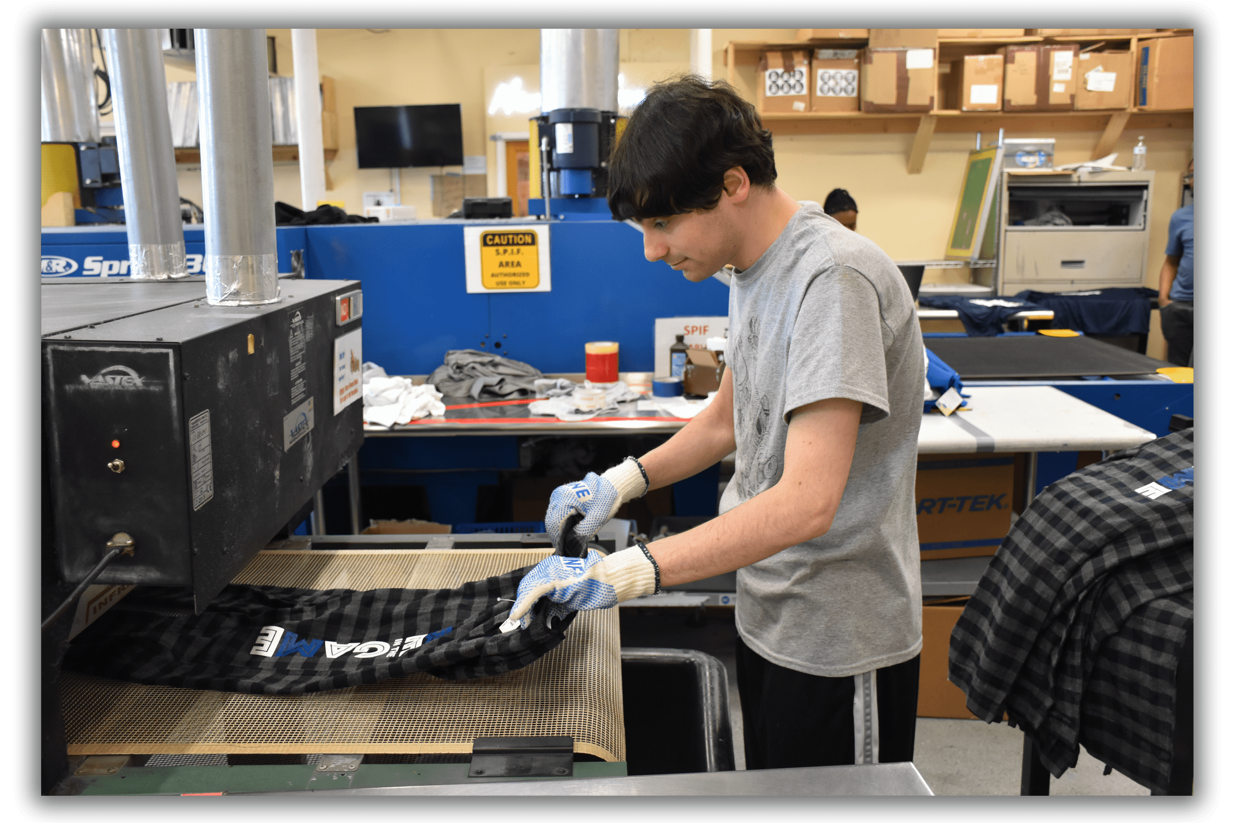 Person operating a screen printing machine to print designs on garments in a workshop.